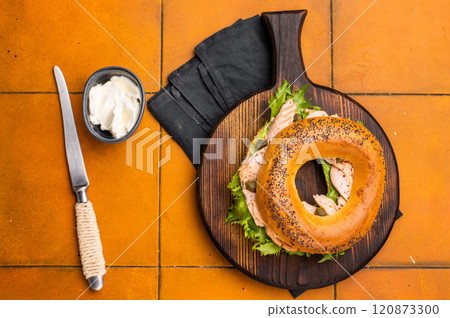 Breakfast Bagel with smoked salmon, lettuce and cream cheese on a wooden board. orange background. top view Breakfast Bagel with smoked salmon, lettuce and cream cheese on a wooden board. orange background. top view 120873300