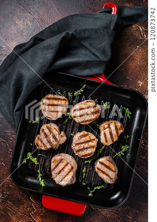 Fried pork medallions steaks from tenderloin meat on a grill skillet. Dark background. Top view Fried pork medallions steaks from tenderloin meat on a grill skillet. Dark background. Top view 120873742