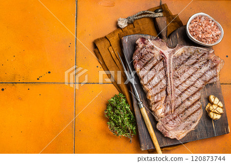 BBQ Roast T bone or Porterhouse beef meat Steak on a wooden board with spices. Orange background. Top view. Copy space 120873744