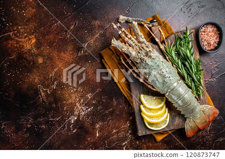 Fresh Spiny lobster on a wooden cutting board with herbs for cooking, raw seafood. Dark background. Top view. Copy space 120873747
