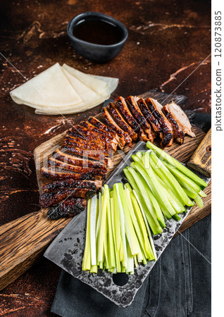 Sliced Peking Duck served with cucumber, green onion, and wheaten chinese pancakes on a meat cleaver. Dark background. Top view 120873885