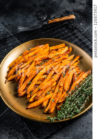 Baked sweet potato fries on a plate with herbs. Black background. Top view 120873917