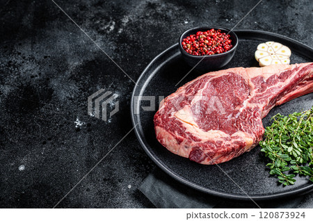 Dry aged cowboy or rib eye steak, raw beef meat with herbs. Black background. Top view. Copy space 120873924