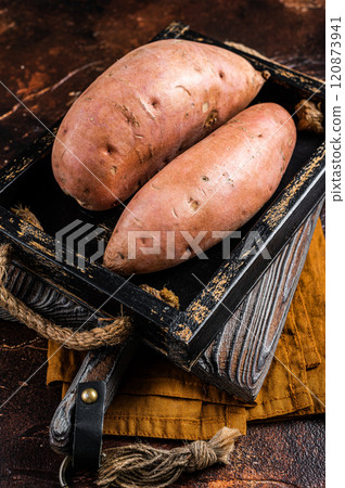 Raw sweet potatoes in a wooden tray, fresh batata. Dark background. Top view 120873941