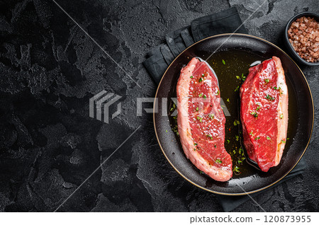 Raw marbled beef meat steak marinated with olive oil, thyme, salt and pepper. Black background. Top view. Copy space 120873955