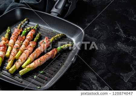 Fried bacon wrapped asparagus in a grill skillet. Black background. Top view. Copy space 120874047