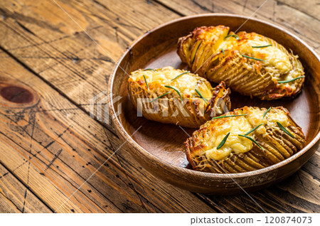 Hasselback potatoes with cheese, garlic and herbs. Wooden background. Top view. Copy space Hasselback potatoes with cheese, garlic and herbs. Wooden background. Top view. Copy space 120874073