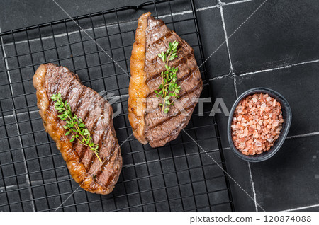 Grilled top sirloin or cup rump beef meat steak on a rack. Black background. Top view Grilled top sirloin or cup rump beef meat steak on a rack. Black background. Top view 120874088