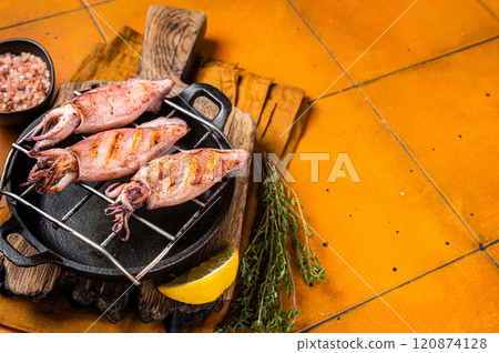 Grilled squid, calamary on a hot flaming. Orange background. Top view. Copy space Grilled squid, calamary on a hot flaming. Orange background. Top view. Copy space 120874128