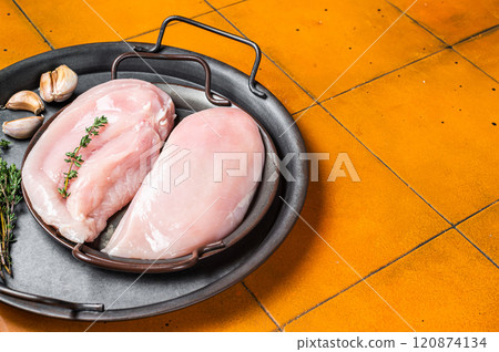 Raw chicken breast fillet in a steel tray with thyme and garlic. Orange background. Top view. Copy space Raw chicken breast fillet in a steel tray with thyme and garlic. Orange background. Top view. Copy space 120874134