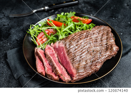 Grilled medium rare flank beef steak with salad in a plate. Black background. Top view 120874140