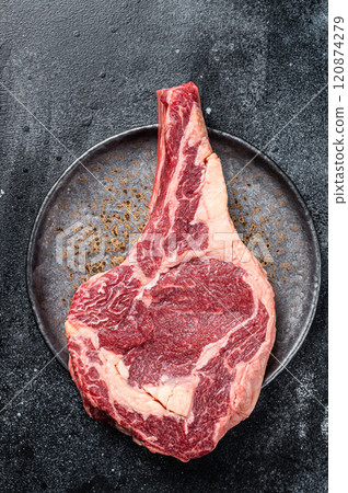 Raw cowboy steak, rib eye steak with bone, beef marbled meat on butcher cutting board. Black background. Top view 120874279