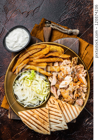 Turkish Doner kebab or gyros on a plate with french fries, vegetables and salad. Dark background. Top view Turkish Doner kebab or gyros on a plate with french fries, vegetables and salad. Dark background. Top view 120874286