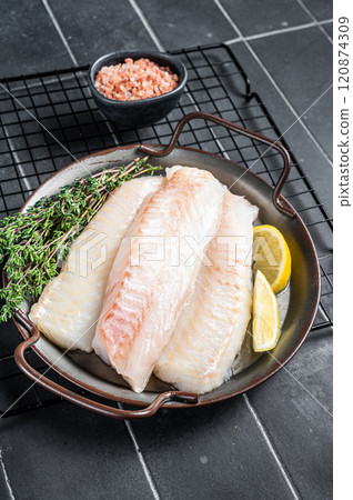 Fresh raw cod fish fillets with herbs served on steel tray. Black background. Top view 120874309