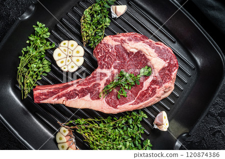 Ready for cooking Raw cowboy or rib eye steak in a grill skillet. Black background. Top view 120874386