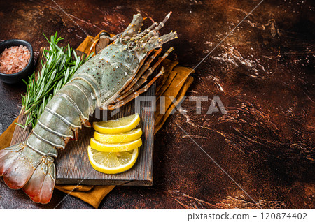 Fresh Spiny lobster on a wooden cutting board with herbs for cooking, raw seafood. Dark background. Top view. Copy space 120874402