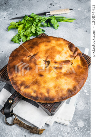 Ossetian pie with beef meat and herbs on wooden board. Gray background. Top view 120874412
