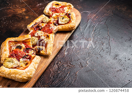 Baked Puff pastry tart pizza with artichoke, mozzarella, tomatoes and cheese sliced on a wooden board. Dark background. Top view. Copy space Baked Puff pastry tart pizza with artichoke, mozzarella, tomatoes and cheese sliced on a wooden board. Dark background. Top view. Copy space 120874458