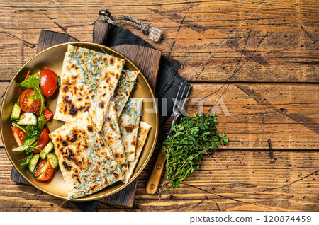 Gozleme flatbread with greens and vegetable salad on garnish. Wooden background. Top view. Copy space 120874459