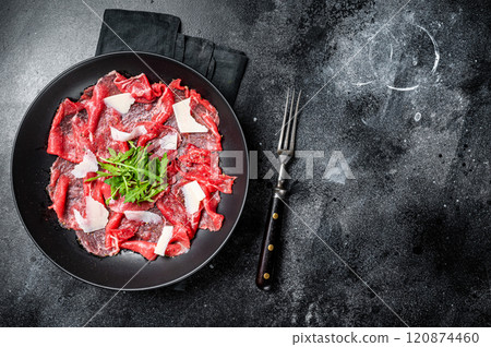 Beef Carpaccio cold appetizer with parmesan and arugula on a plate. Black background. Top view. Copy space Beef Carpaccio cold appetizer with parmesan and arugula on a plate. Black background. Top view. Copy space 120874460