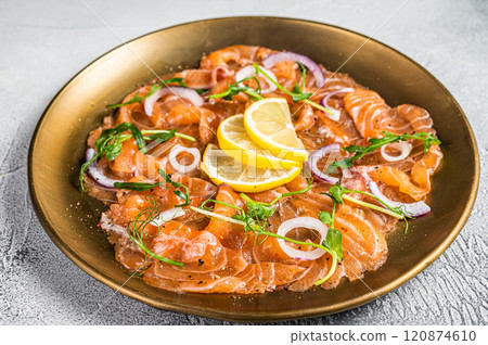 Fresh raw salmon carpaccio slices with onion and arugula served on a plate. White background. Top view 120874610