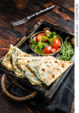 Baked Gozleme flatbread with greens in a box with vegetable salad. Wooden background. Top view 120874626