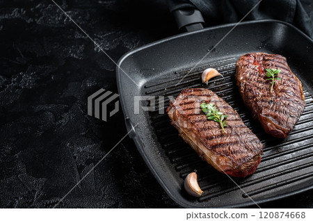 Grilled Top Blade or flat iron roast beef meat steaks on a skillet. Black background. Top View. Copy space 120874668