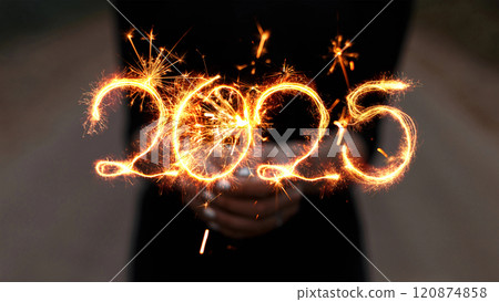Girl holds a sparkler in her hands and draws 2025 with sparks. New Year 2025, creative idea. 120874858