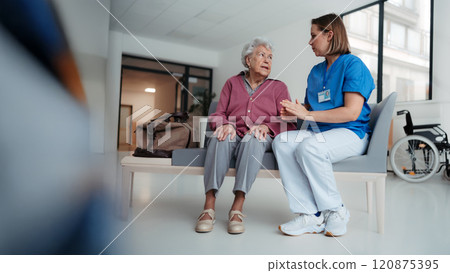 Hospital nurse delivering bed news to family member of patient. Old patient sitting in hospital corridor suffering from pain. 120875395