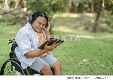 Young Disabled Businessman in Wheelchair Using Tablet for Outdoor Work in a Modern Green Environment 120877162