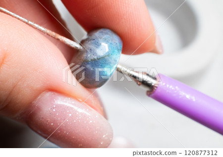 female hands of a jeweler holding a stone, close-up. stone appraiser. checking the quality of products. preparing a stone for making a bracelet 120877312