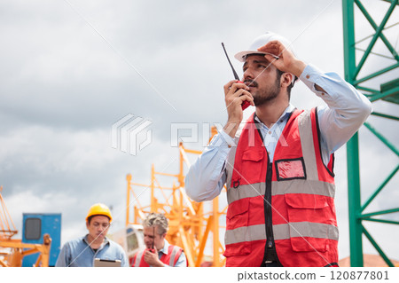 Worker at construction site, communicating with colleague on walkie Talkie. Worker at construction site, communicating with colleague on walkie Talkie. 120877801