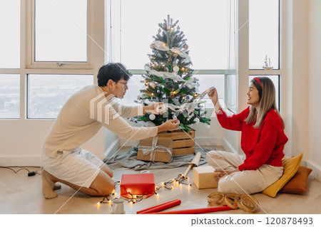 Husband and wife couple lover decorating Christmas tree together while the man helping woman packing decoration boxes. Husband and wife couple lover decorating Christmas tree together while the man helping woman packing decoration boxes. 120878493