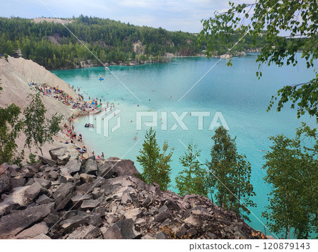 Many people swimming in the blue water near the sandy shore in a flooded quarry on a summer day. Beautiful blue water of large lake and many people swimming near the sandy shore of the slope. Top view 120879143