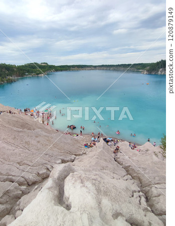 Many people swimming in the blue water near the sandy shore in a flooded quarry on a summer day. Beautiful blue water of large lake and many people swimming near the sandy shore of the slope. Top view Many people swimming in the blue water near the sandy shore in a flooded quarry on a summer day. Beautiful blue water of large lake and many people swimming near the sandy shore of the slope. Top view 120879149