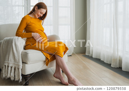 Pregnancy motherhood people expectation future. Pregnant woman with big belly sitting on chair near window at home. Girl hugging her tummy enjoying pregnancy. Maternity tenderness parenthood new life 120879338