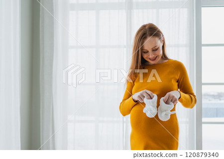 Pregnancy motherhood people expectation future. Pregnant woman with big belly holding newborn baby booties smiling at home. Young mom enjoying pregnancy. Maternity tenderness parenthood new life 120879340