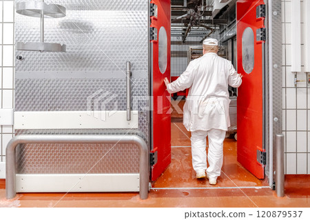 Butcher opening red door entering cold storage room in meat processing plant 120879537