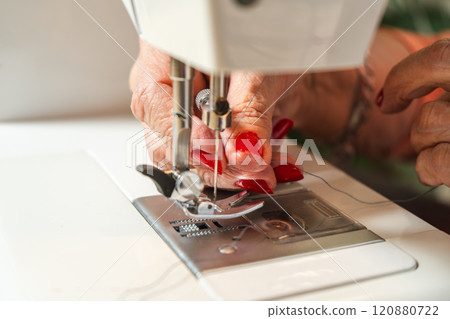 Hands of an older woman threading the sewing machine needle before starting. 120880722