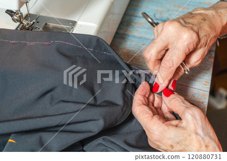 Hands of a eldlerly seamstress sewing a pair of pants on a sewing machine. 120880731
