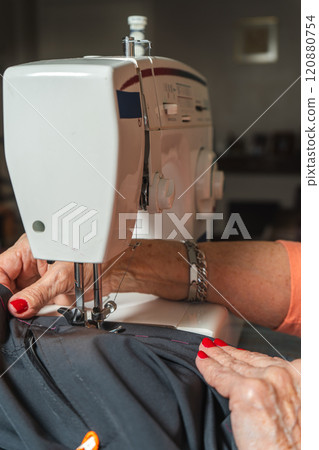 Hands of a eldlerly seamstress sewing a pair of pants on a sewing machine. Hands of a eldlerly seamstress sewing a pair of pants on a sewing machine. 120880754