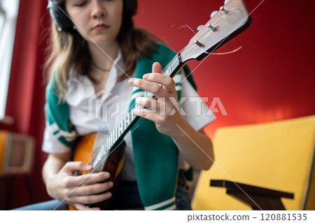 Woman practices balalaika chords wearing headphones while playing in rhythm. Music practice at home 120881535
