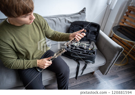 Man hands puts disassembled black clarinet in special case, inspects parts of flute after playing it 120881594