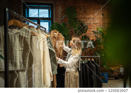 Interested woman chooses clothes to buy in store, holds hanger with dress in hands, looks price tag 120881607