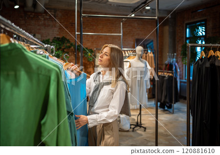 Pleased woman shopaholic examines clothing with interest before purchase, making choice in boutique. 120881610
