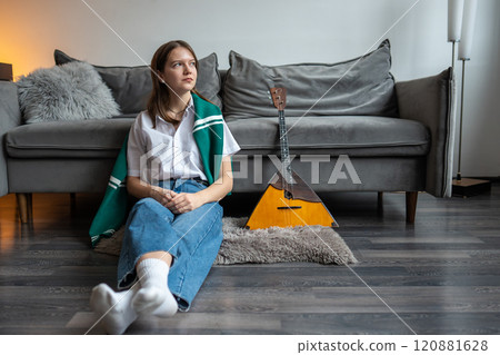 Thoughtful young woman resting after playing on Russian balalaika at home, sitting on floor at home 120881628