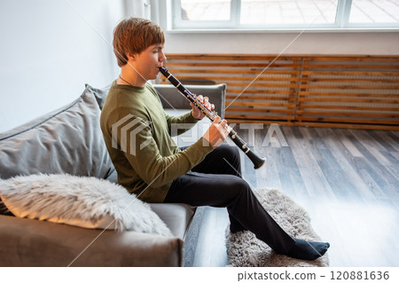 Clarinet player. Man clarinetist playing flute woodwind music instrument sitting on couch at home 120881636