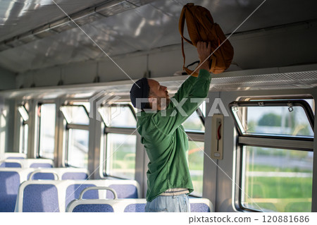 Man tourist lifts backpack onto overhead luggage rack in train. Solo travel and transit convenience 120881686