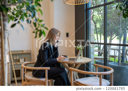 Thoughtful woman in business suit calling on phone sits with laptop in cafe pensive looks to window Thoughtful woman in business suit calling on phone sits with laptop in cafe pensive looks to window 120881785