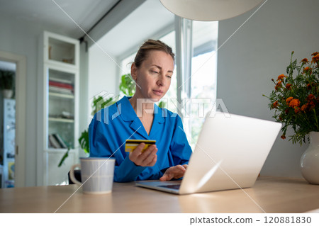 Focused woman on laptop uses credit card for online transaction, lost in heavy spending. Credit debt 120881830